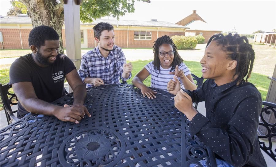  A group of four students relaxing and laughing at an outdoor table. 